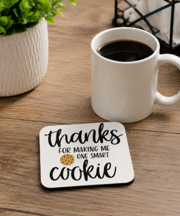 Teacher appreciation coaster featuring the quote Thanks for Making Me One Smart Cookie with a cookie illustration, displayed beside a drinking glass on a desk surface.